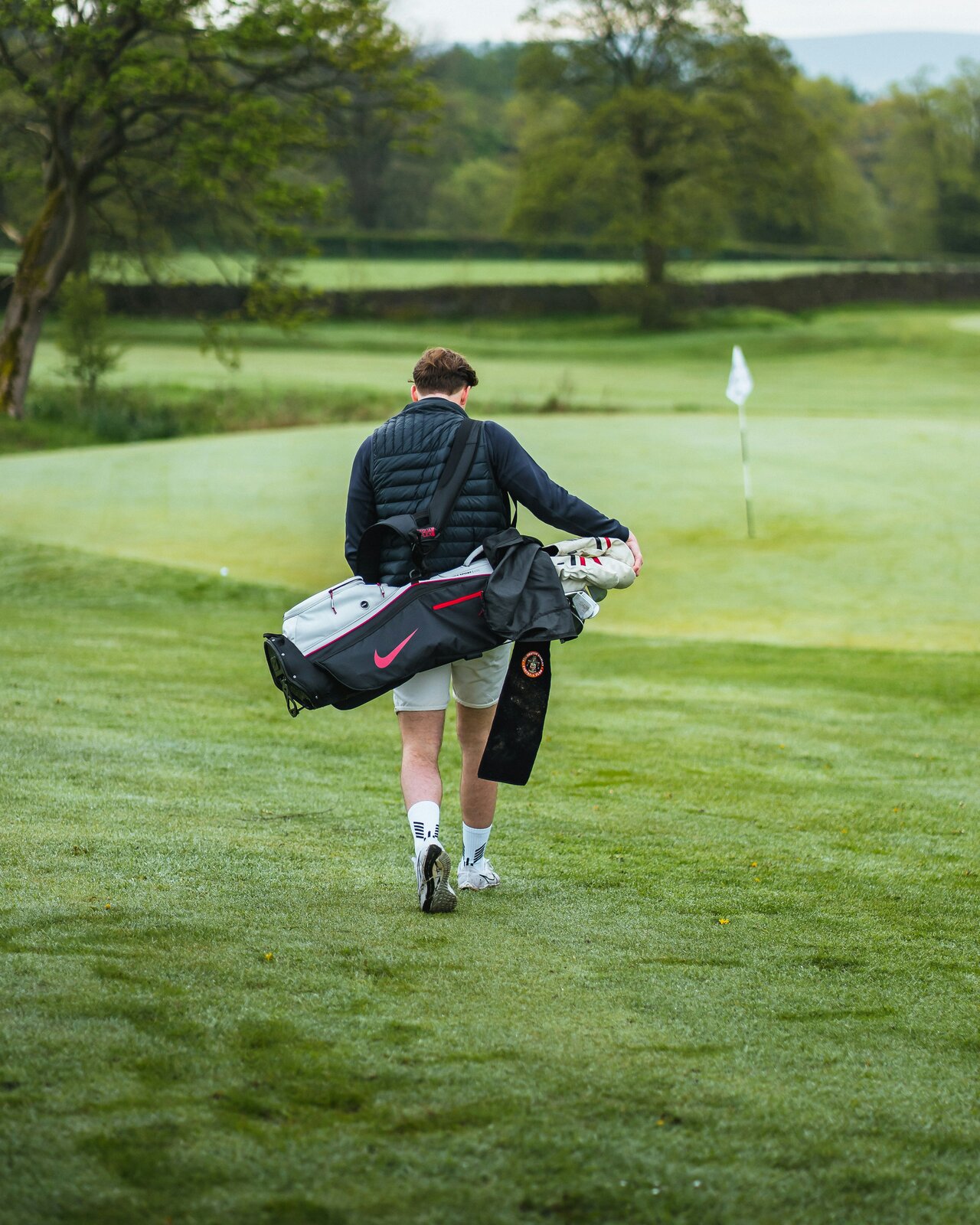 a golfer walking the fairway, carry bag on shoulder, flagstick ahead